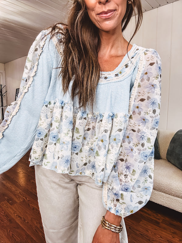 Light blue ribbed texture long sleeved top with sheer blue and green floral inserts at sleeves and ruffled hem with lace embroidery, elastic cuffs and round neck with lace and embroidery trim.