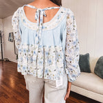 Light blue ribbed texture long sleeved top with sheer blue and green floral inserts at sleeves and ruffled hem with lace embroidery, elastic cuffs and round neck with lace and embroidery trim.