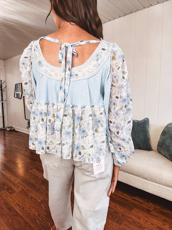 Light blue ribbed texture long sleeved top with sheer blue and green floral inserts at sleeves and ruffled hem with lace embroidery, elastic cuffs and round neck with lace and embroidery trim.