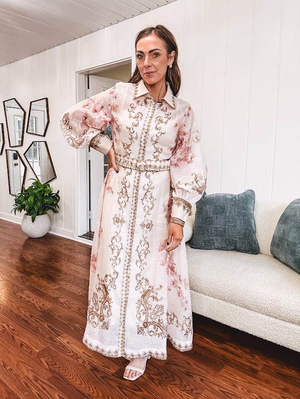 Tan slip dress with long sleeved organza overlay featuring muted florals in pink and cream with vintage inspired design, pearl and gold buttons down the front, cuffs and matching fabric belt with gold accent.