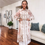Tan slip dress with long sleeved organza overlay featuring muted florals in pink and cream with vintage inspired design, pearl and gold buttons down the front, cuffs and matching fabric belt with gold accent.