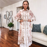 Tan slip dress with long sleeved organza overlay featuring muted florals in pink and cream with vintage inspired design, pearl and gold buttons down the front, cuffs and matching fabric belt with gold accent.