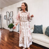 Tan slip dress with long sleeved organza overlay featuring muted florals in pink and cream with vintage inspired design, pearl and gold buttons down the front, cuffs and matching fabric belt with gold accent.