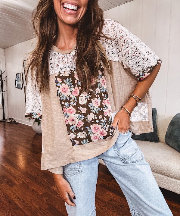 Lightweight ribbed textured taupe top with lace at the yoke and sides and a brown and pink and blue floral patch in the front at at the cuffs of the short sleeves. Oversized.