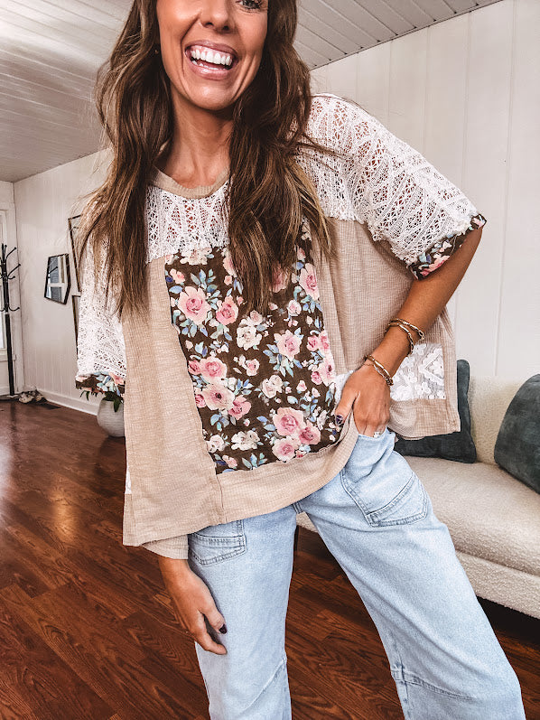 Lightweight ribbed textured taupe top with lace at the yoke and sides and a brown and pink and blue floral patch in the front at at the cuffs of the short sleeves. Oversized.