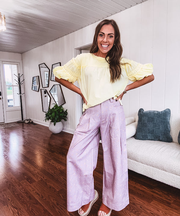 Light purple denim-like wide leg pants with elastic back waist, button and zipper closure and pleating at the front, with pockets and small pink and yellow florals throughout.