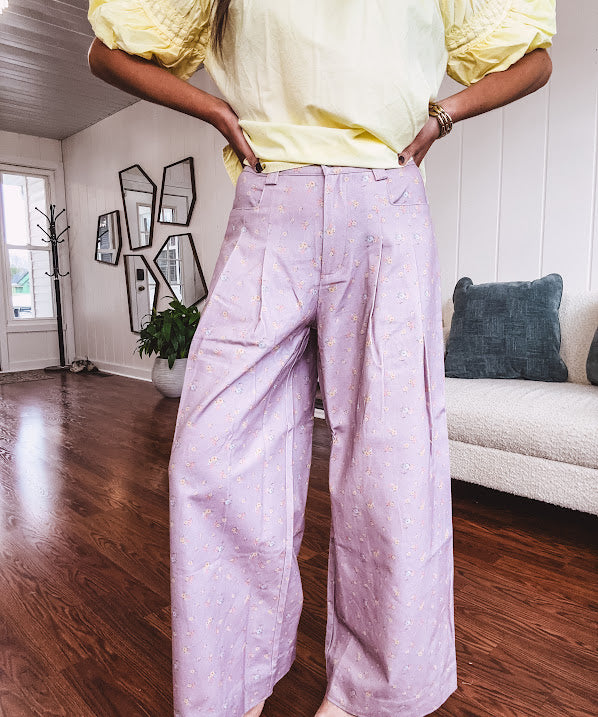 Light purple denim-like wide leg pants with elastic back waist, button and zipper closure and pleating at the front, with pockets and small pink and yellow florals throughout.