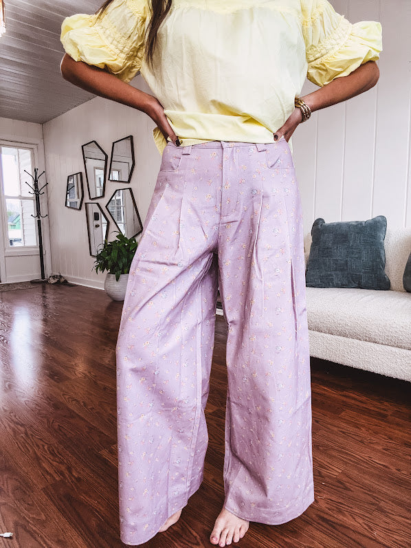 Light purple denim-like wide leg pants with elastic back waist, button and zipper closure and pleating at the front, with pockets and small pink and yellow florals throughout.