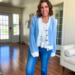 Light blue cable knit cardigan with white trim and flutter hem and cuffs with metal floral buttons down the front.