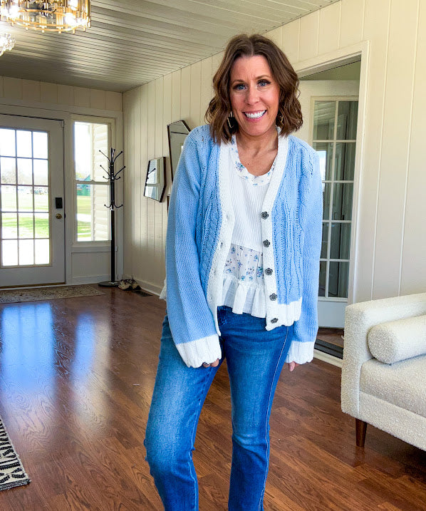 Light blue cable knit cardigan with white trim and flutter hem and cuffs with metal floral buttons down the front.