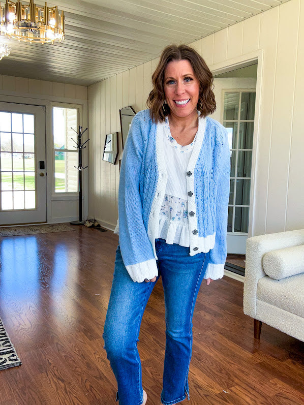 Light blue cable knit cardigan with white trim and flutter hem and cuffs with metal floral buttons down the front.