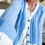 Light blue cable knit cardigan with white trim and flutter hem and cuffs with metal floral buttons down the front.
