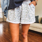 Thin, soft white elastic waist shorts with small blue and green florals throughout with pockets and white trim at the hem.