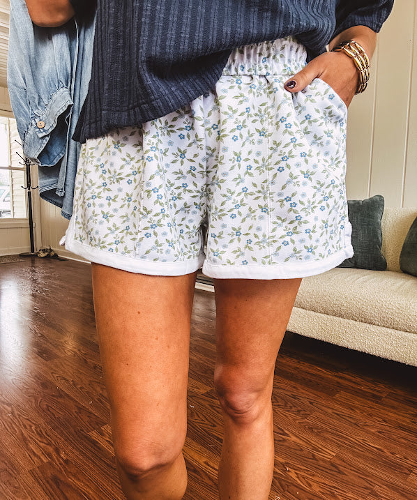 Thin, soft white elastic waist shorts with small blue and green florals throughout with pockets and white trim at the hem.