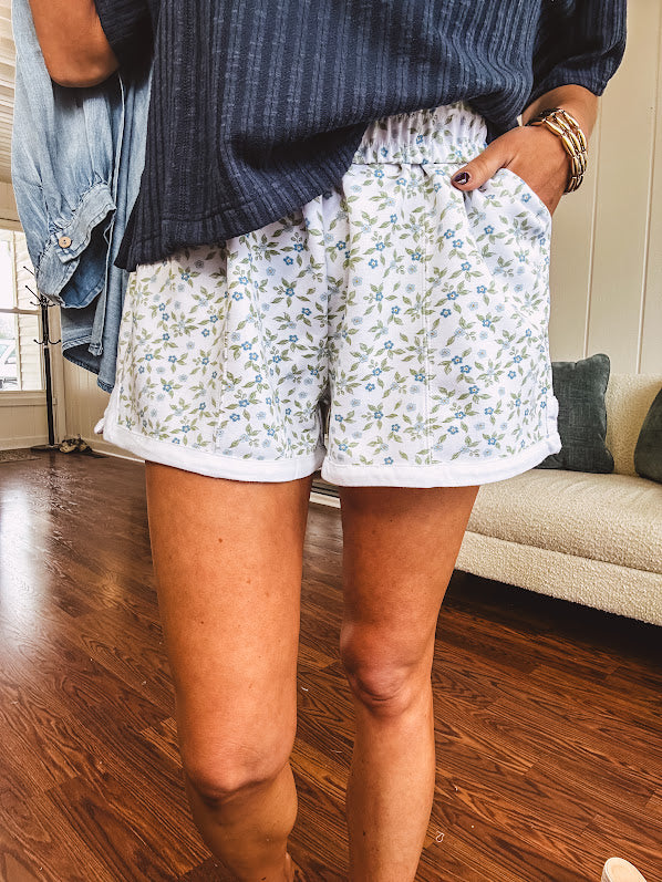 Thin, soft white elastic waist shorts with small blue and green florals throughout with pockets and white trim at the hem.