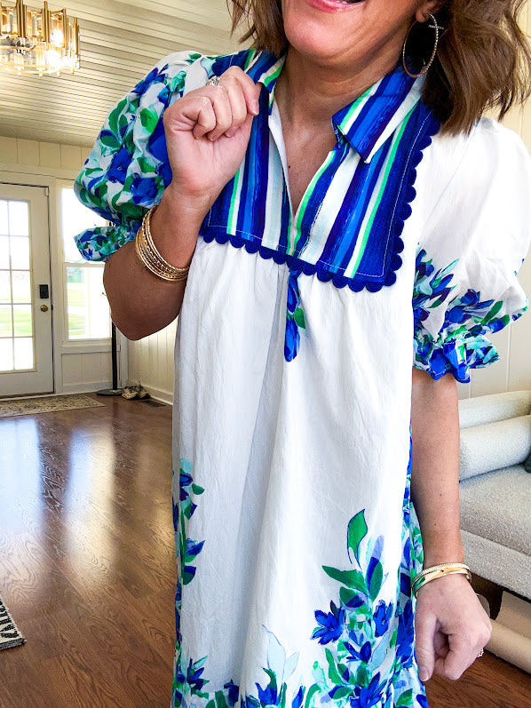 Fully lined linen-like short white dress with royal blue, lime green and purple stripes at the yoke and florals throughout with rickrack trim at the yoke and collar with V neck. Has pockets.
