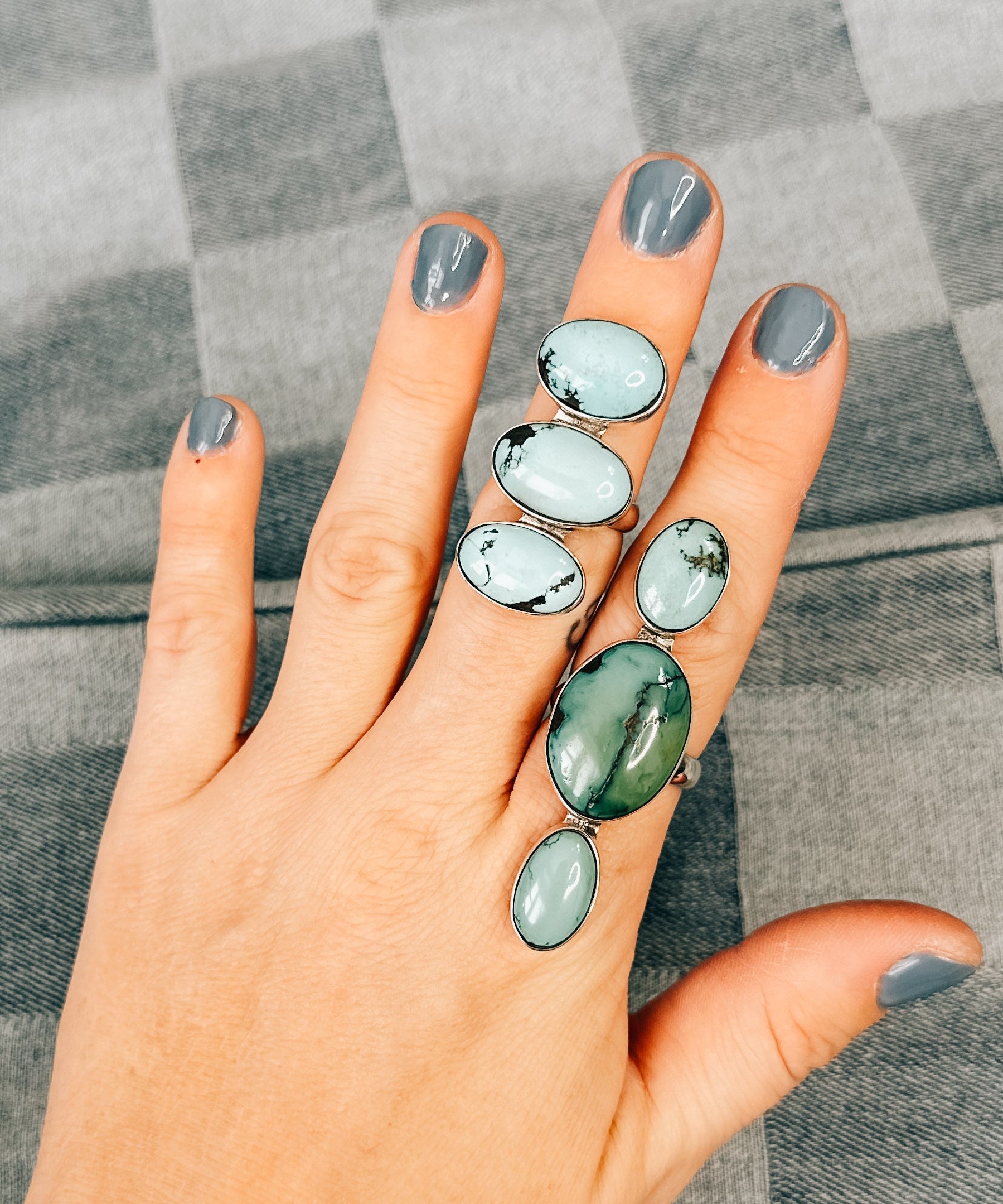 A hand displaying a triple ring with Kingman Turquoise stones, set in silver, on a textured grey background.