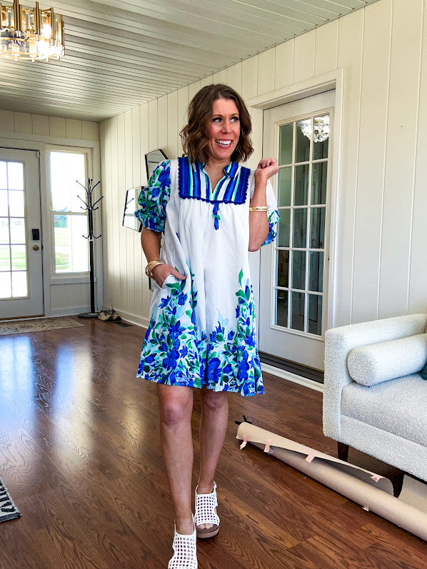Fully lined linen-like short white dress with royal blue, lime green and purple stripes at the yoke and florals throughout with rickrack trim at the yoke and collar with V neck. Has pockets.