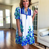 Fully lined linen-like short white dress with royal blue, lime green and purple stripes at the yoke and florals throughout with rickrack trim at the yoke and collar with V neck. Has pockets.
