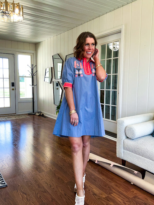 Slate blue dress with puffed, cuffed short sleeves, pockets, a contrasting coral collar and V neck, cuffs and trim and coral and pink embroidery at the yoke.