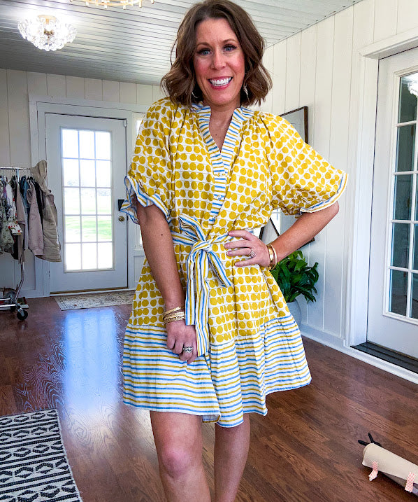 Fully lined short sleeved short dress with mustard polka dots trimmed in dusty blue, mustard and cream stripes at the mock neck and placket, ruffled cuffs, belt and hem.