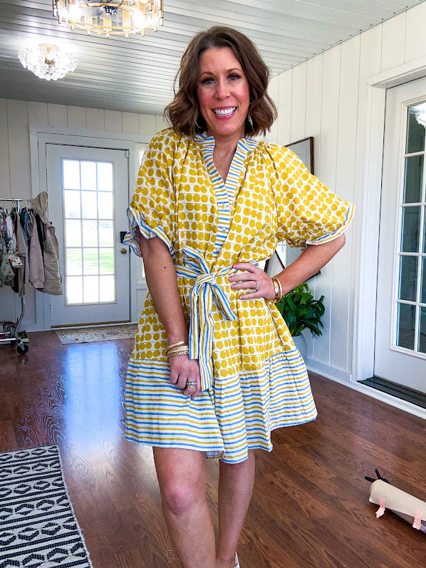 Fully lined short sleeved short dress with mustard polka dots trimmed in dusty blue, mustard and cream stripes at the mock neck and placket, ruffled cuffs, belt and hem.