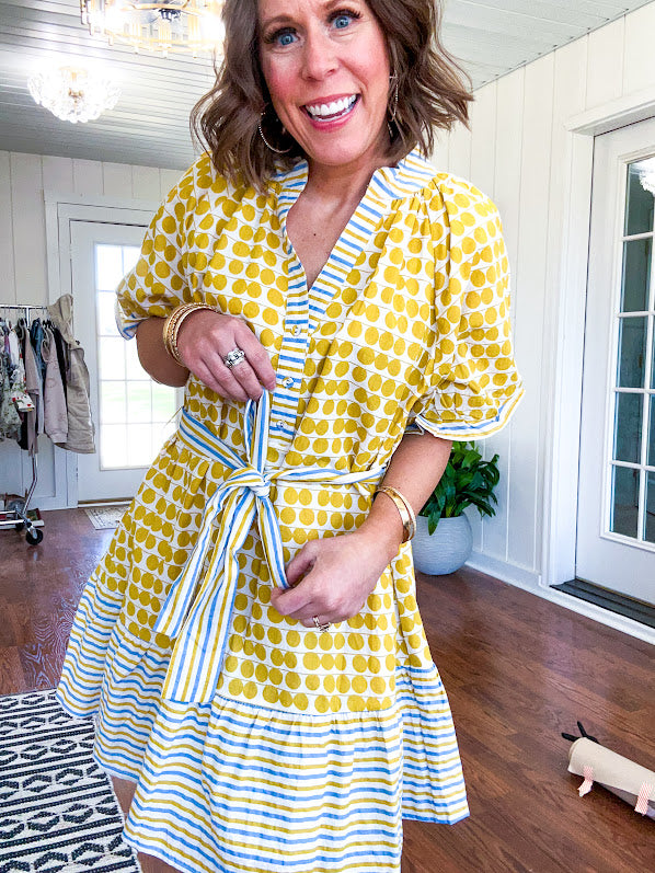 Fully lined short sleeved short dress with mustard polka dots trimmed in dusty blue, mustard and cream stripes at the mock neck and placket, ruffled cuffs, belt and hem.