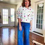 Fully lined off white shirt with 3/4 sleeve with cuffs, a short hemline and eyelet and pink and green floral details throughout, hook and eye closure at the neck.