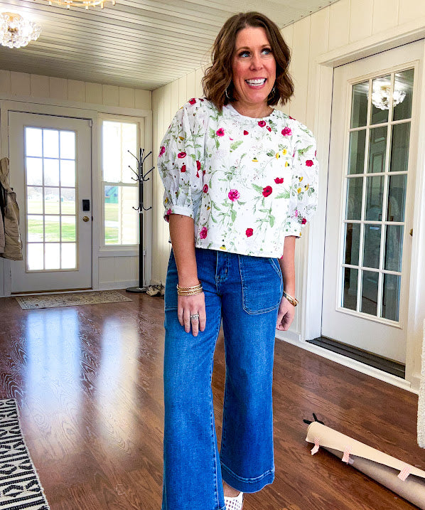 Fully lined off white shirt with 3/4 sleeve with cuffs, a short hemline and eyelet and pink and green floral details throughout, hook and eye closure at the neck.