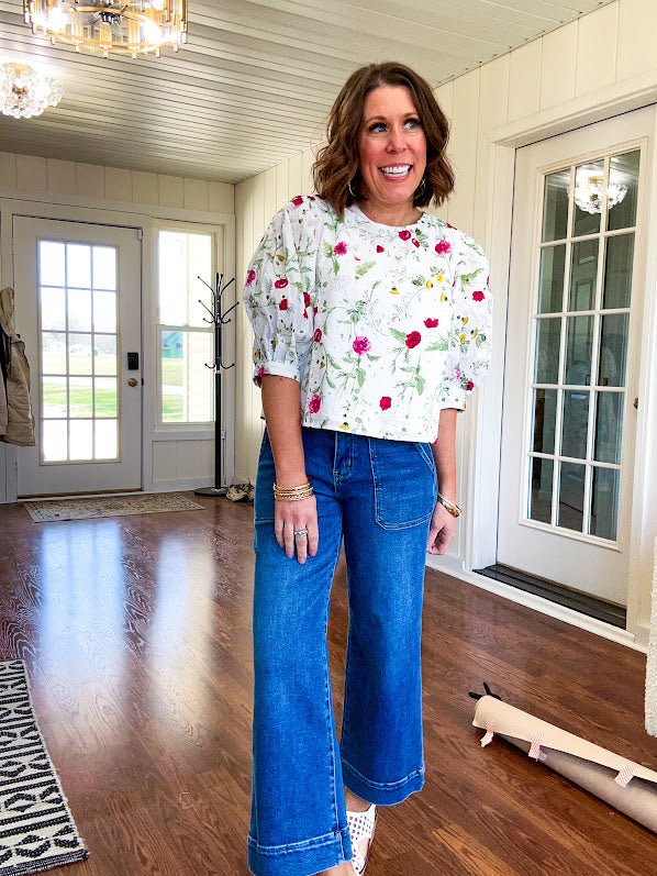 Fully lined off white shirt with 3/4 sleeve with cuffs, a short hemline and eyelet and pink and green floral details throughout, hook and eye closure at the neck.
