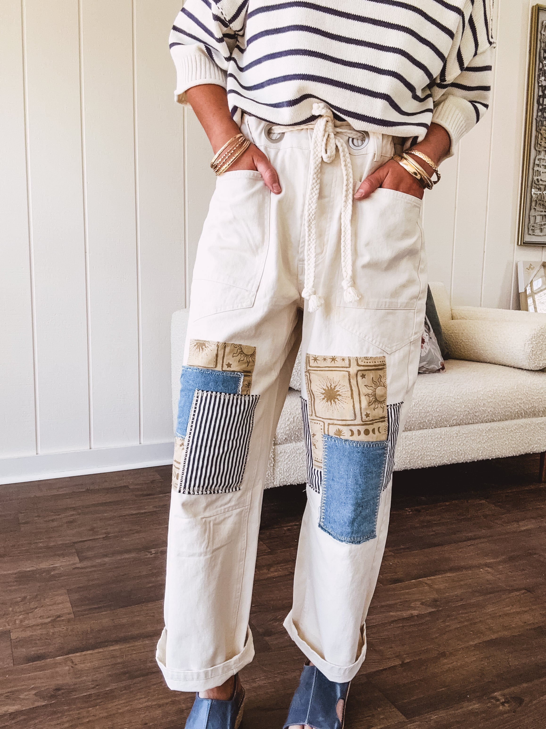 Creamy wide-leg pants, denim-like cotton material with silver grommet belt loops and a coordinating rope belt, button fly and oversized pockets, and striped patchwork in sand, denim, navy, and white creates visual interest down the legs.