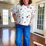 Fully lined off white shirt with 3/4 sleeve with cuffs, a short hemline and eyelet and pink and green floral details throughout, hook and eye closure at the neck.