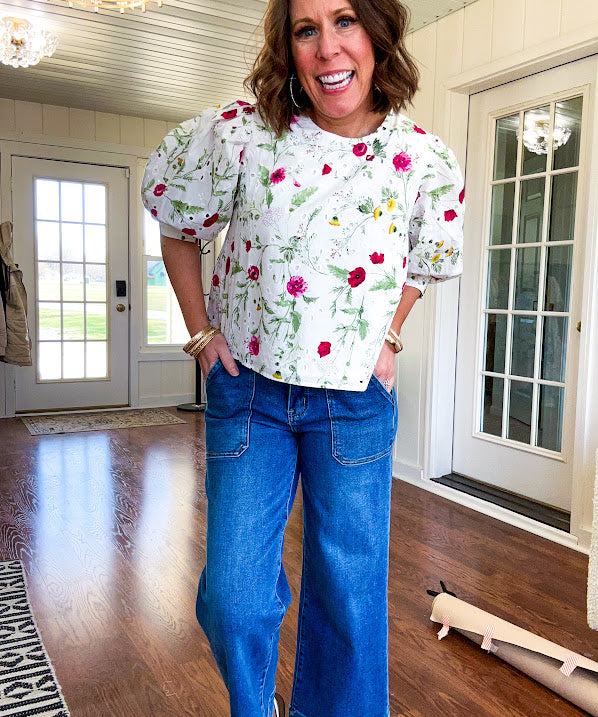 Fully lined off white shirt with 3/4 sleeve with cuffs, a short hemline and eyelet and pink and green floral details throughout, hook and eye closure at the neck.