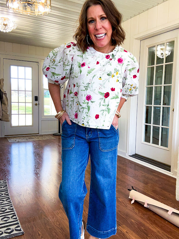 Fully lined off white shirt with 3/4 sleeve with cuffs, a short hemline and eyelet and pink and green floral details throughout, hook and eye closure at the neck.