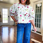 Fully lined off white shirt with 3/4 sleeve with cuffs, a short hemline and eyelet and pink and green floral details throughout, hook and eye closure at the neck.