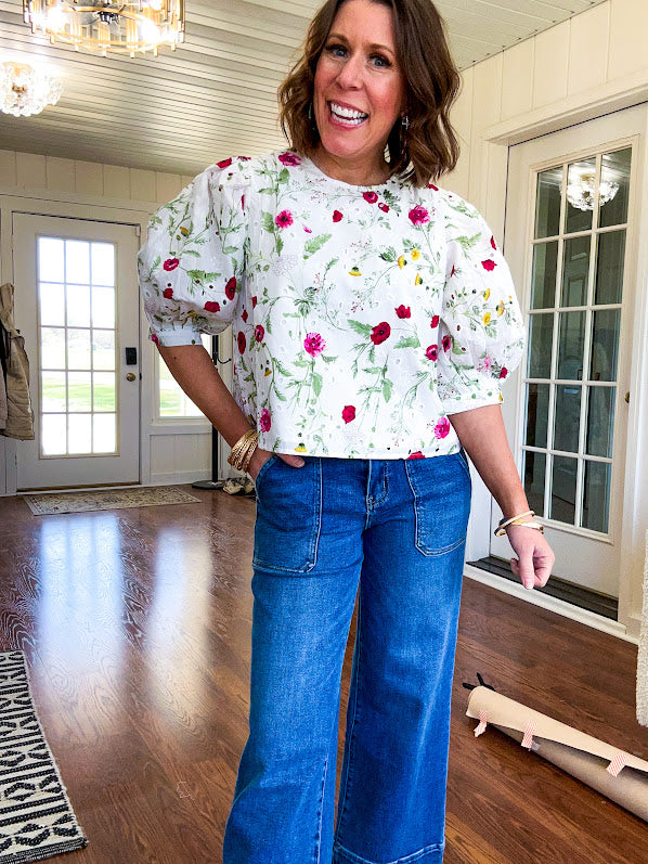 Fully lined off white shirt with 3/4 sleeve with cuffs, a short hemline and eyelet and pink and green floral details throughout, hook and eye closure at the neck.