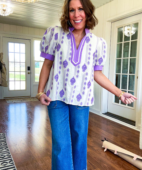 Fully lined lavender and cream blouse with lavender trim at the mock collar and V neck and cuffs, short puffed sleeves and lavender and cream embroidery throughout in an abstract pattern.