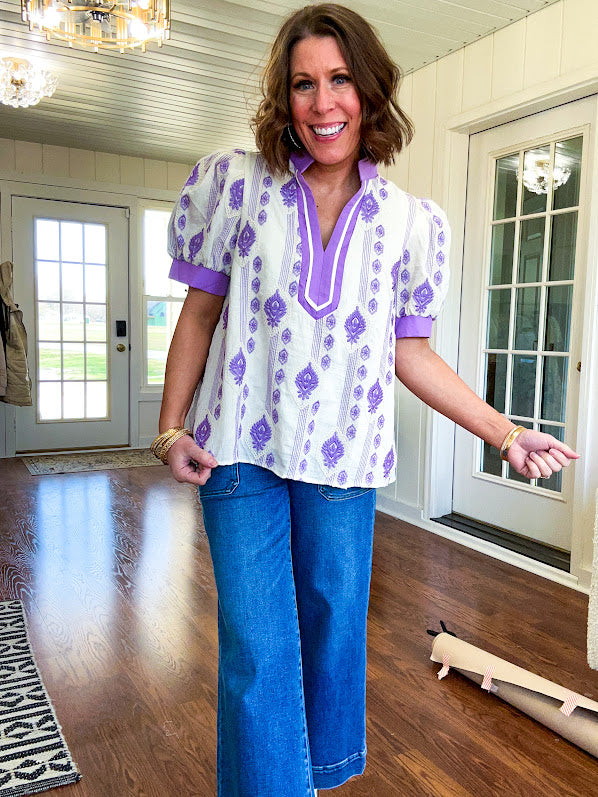 Fully lined lavender and cream blouse with lavender trim at the mock collar and V neck and cuffs, short puffed sleeves and lavender and cream embroidery throughout in an abstract pattern.