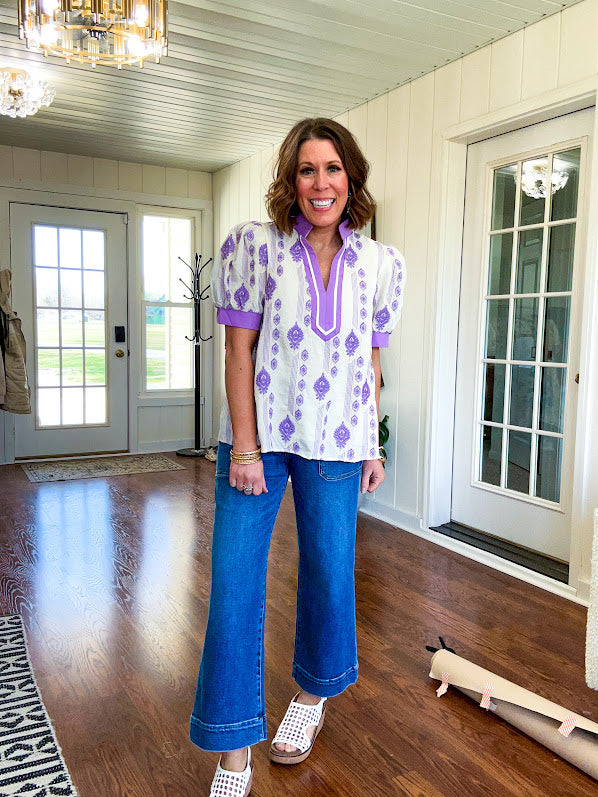 Fully lined lavender and cream blouse with lavender trim at the mock collar and V neck and cuffs, short puffed sleeves and lavender and cream embroidery throughout in an abstract pattern.