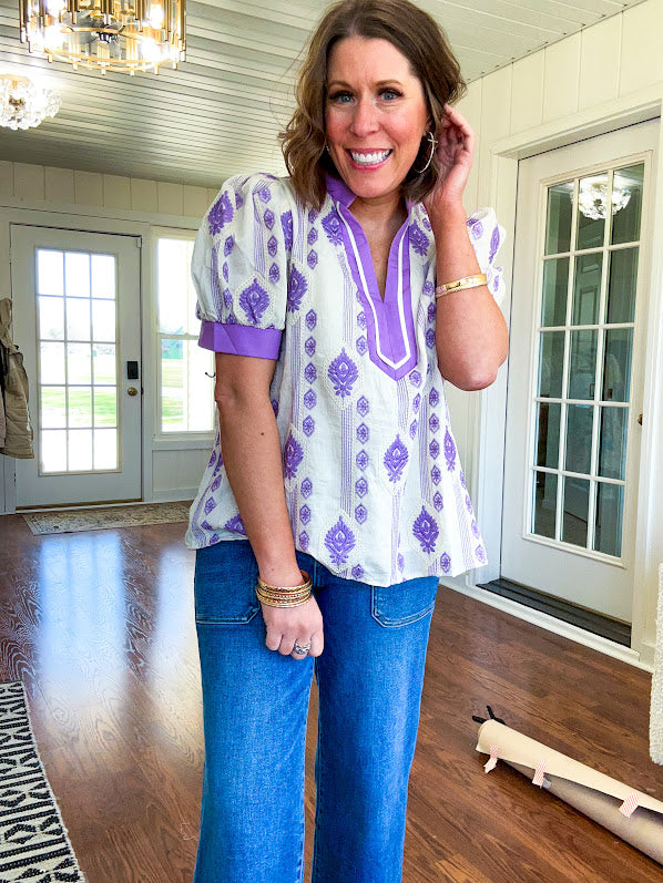 Fully lined lavender and cream blouse with lavender trim at the mock collar and V neck and cuffs, short puffed sleeves and lavender and cream embroidery throughout in an abstract pattern.