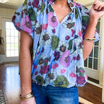 Lined blue flowy bubble hem blouse with mock collar and V neck and bubble short sleeves with purple, sage, olive and pink florals throughout.