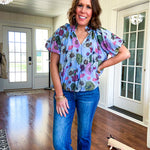 Lined blue flowy bubble hem blouse with mock collar and V neck and bubble short sleeves with purple, sage, olive and pink florals throughout.