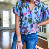 Lined blue flowy bubble hem blouse with mock collar and V neck and bubble short sleeves with purple, sage, olive and pink florals throughout.