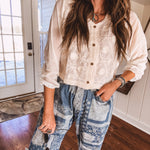 Short sheer beige button down long sleeved top with whimsical embroidery throughout and elastic cuffs.