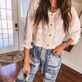 Short sheer beige button down long sleeved top with whimsical embroidery throughout and elastic cuffs.