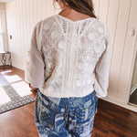 Short sheer beige button down long sleeved top with whimsical embroidery throughout and elastic cuffs.