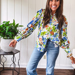 Bright green, orange and blue florals adorn this white button down blouse with a collar, puff sleeves and white eyelet trim throughout.