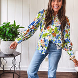 Bright green, orange and blue florals adorn this white button down blouse with a collar, puff sleeves and white eyelet trim throughout.