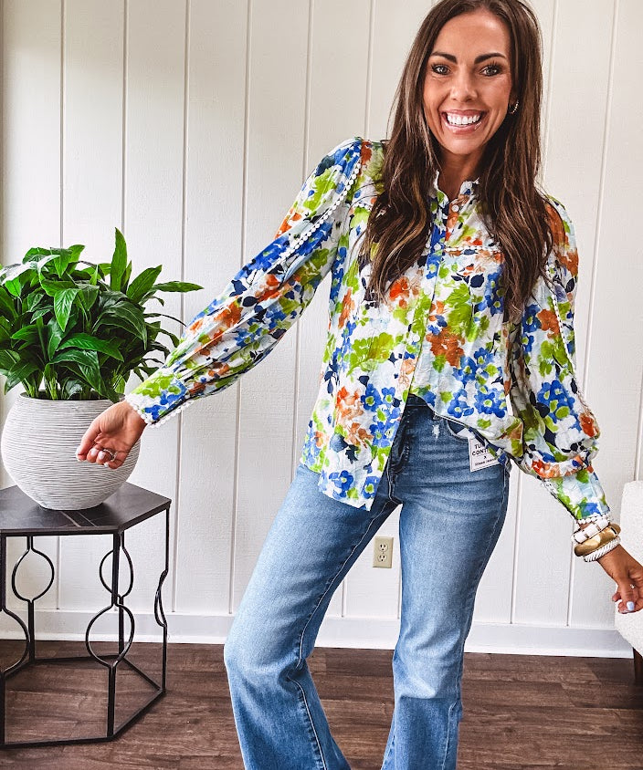 Bright green, orange and blue florals adorn this white button down blouse with a collar, puff sleeves and white eyelet trim throughout.