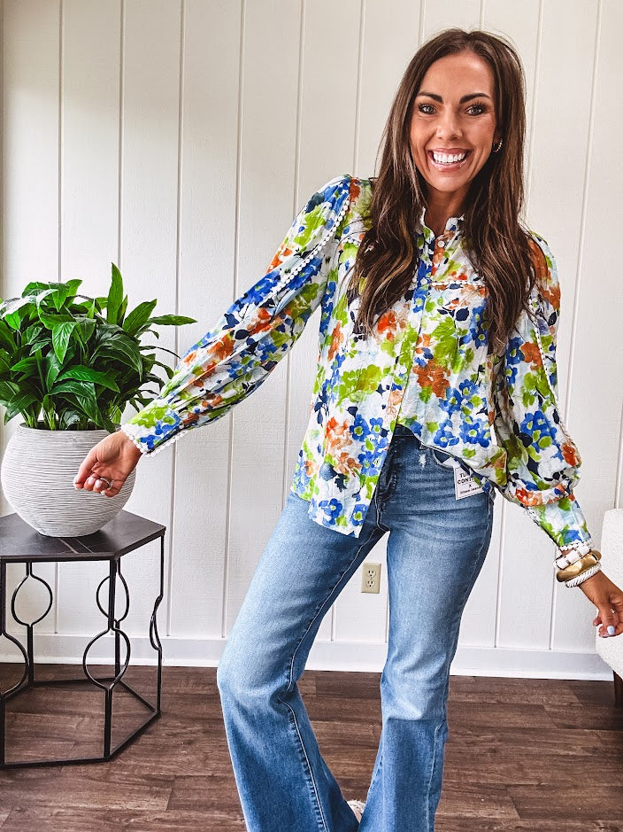 Bright green, orange and blue florals adorn this white button down blouse with a collar, puff sleeves and white eyelet trim throughout.